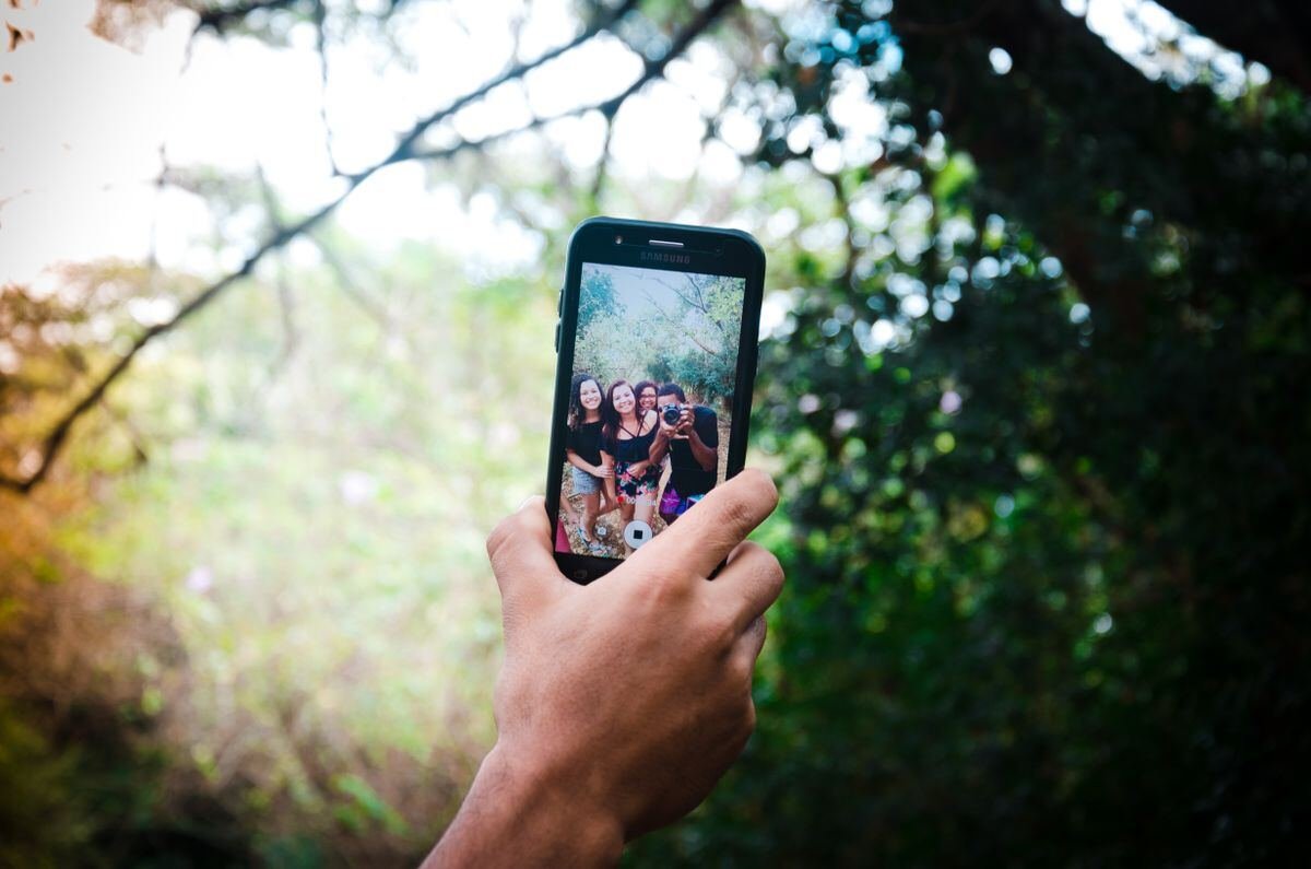 Person holding a smartphone taking a photo, representing TikTok profile picture setup